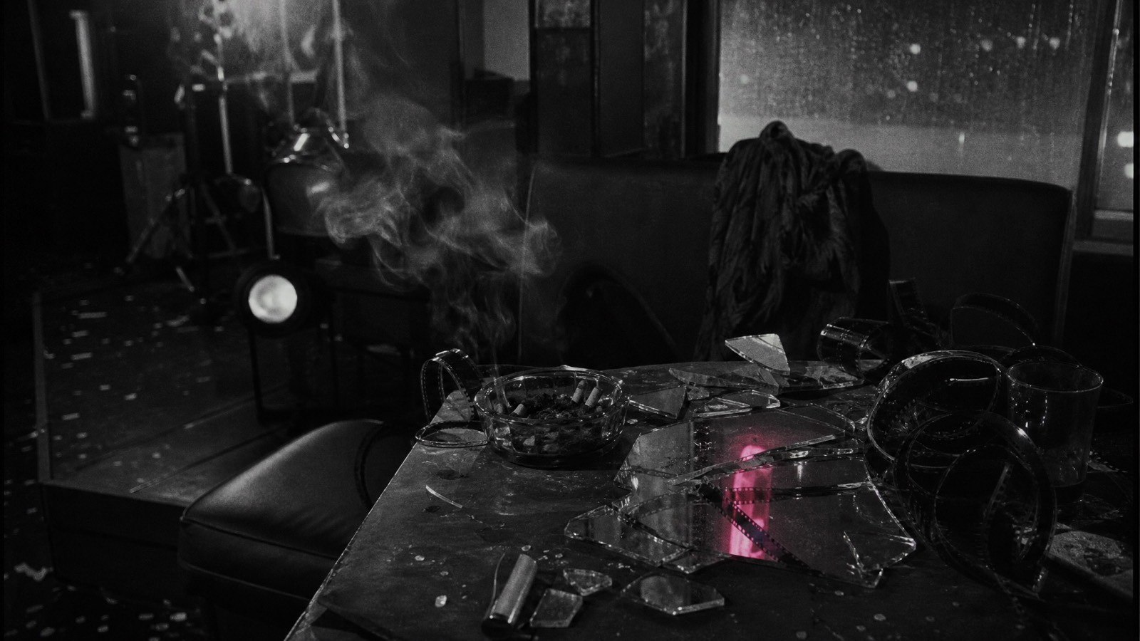Mesa oscura con fragmentos de espejo, humo y tiras de película como residuo del underground de Funeral Parade of Roses.