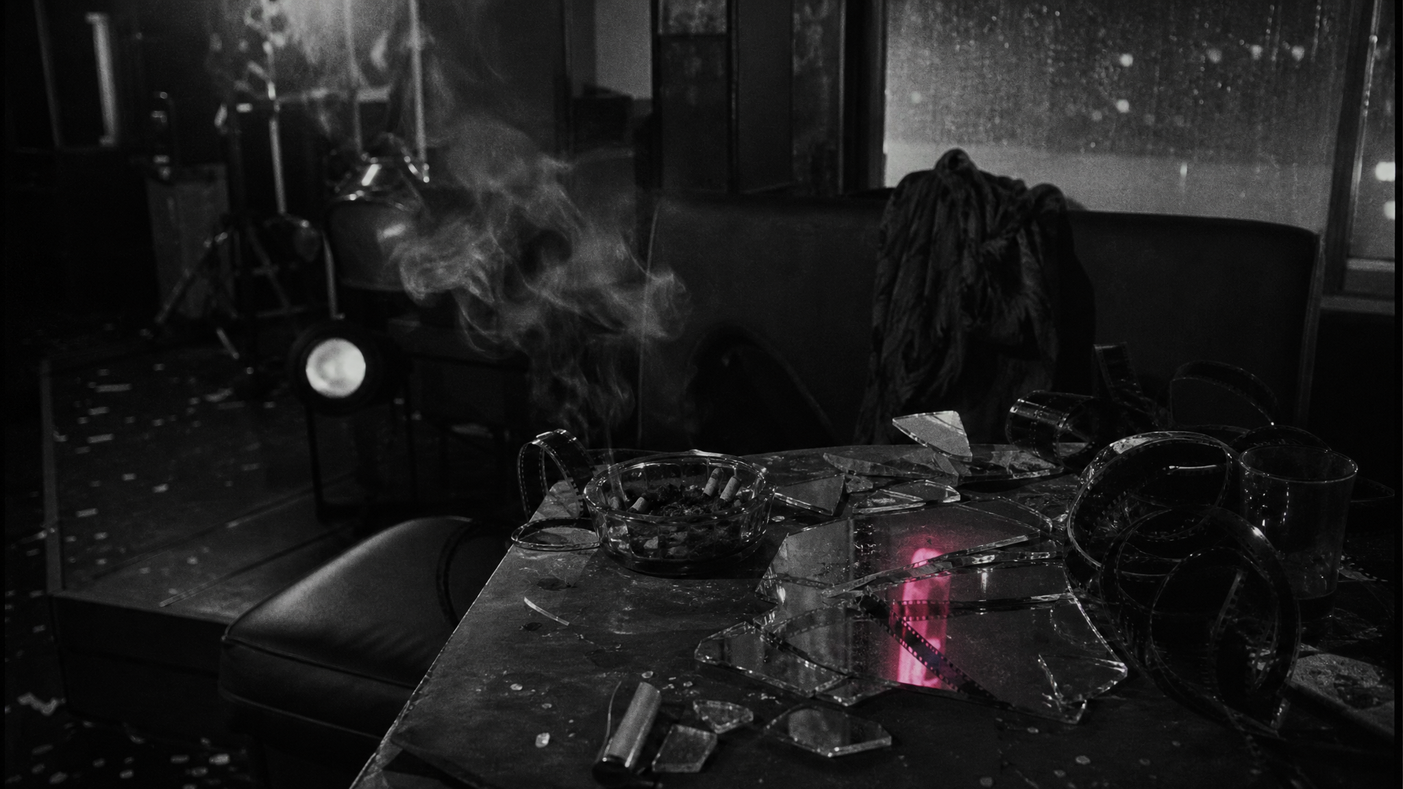 Mesa oscura con fragmentos de espejo, humo y tiras de película como residuo del underground de Funeral Parade of Roses.