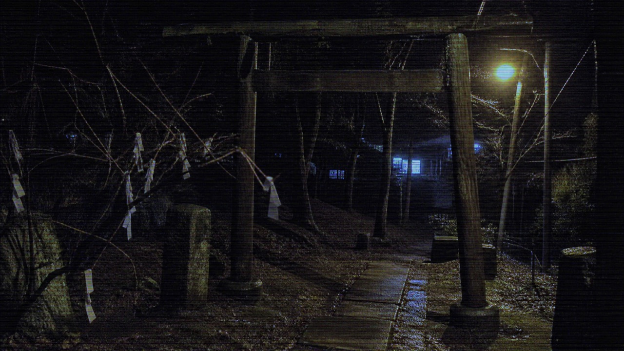 Sendero nocturno hacia un pequeño santuario rural con amuletos y luz azul lejana